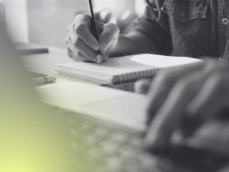 A person at a laptop writing in a notebook