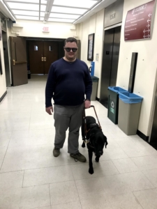 Josh walks down a hallway with his guide dog - a black Lab named York