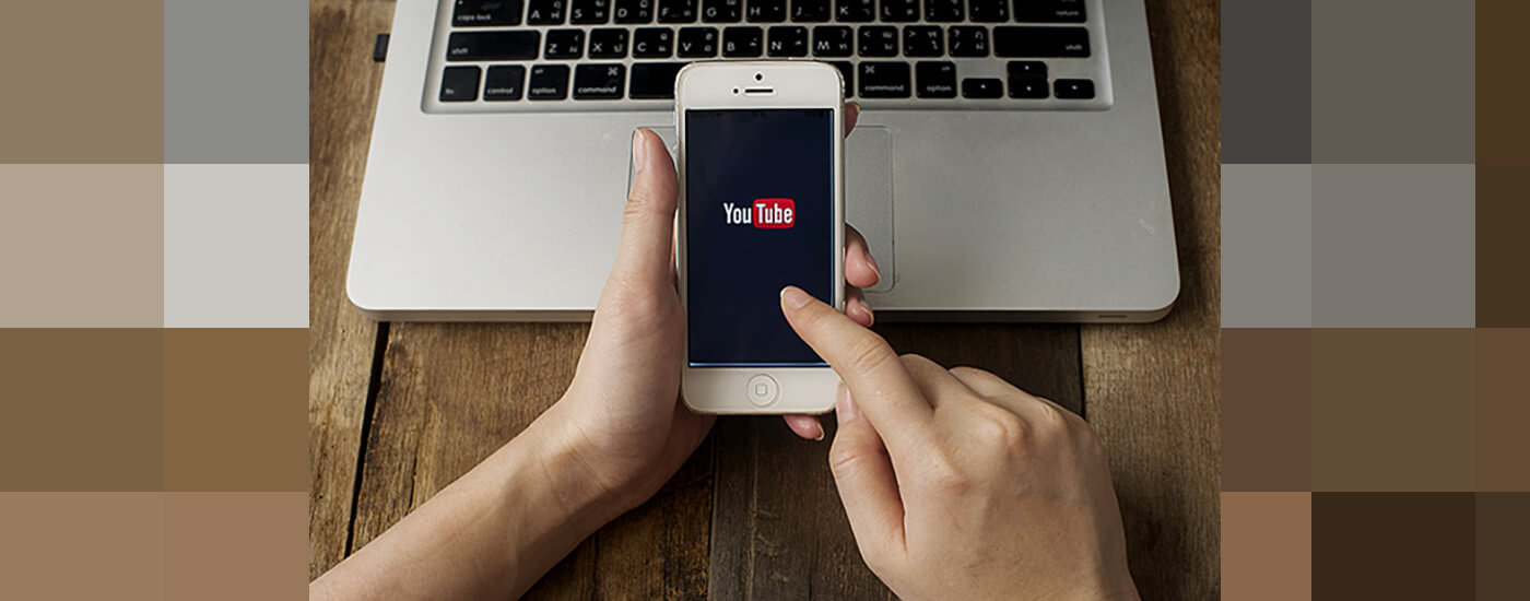 Someone using an iPhone in front of a laptop. The phone's screen has the YouTube logo on it.