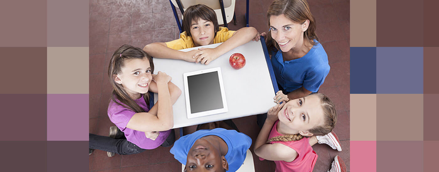 Children sitting around a table with an ipad. The are looking up at the camera smiling.