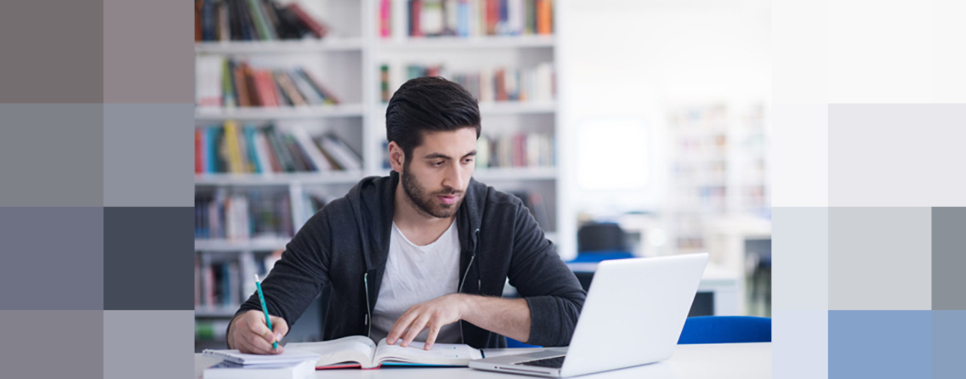 A student taking notes while looking at his laptop