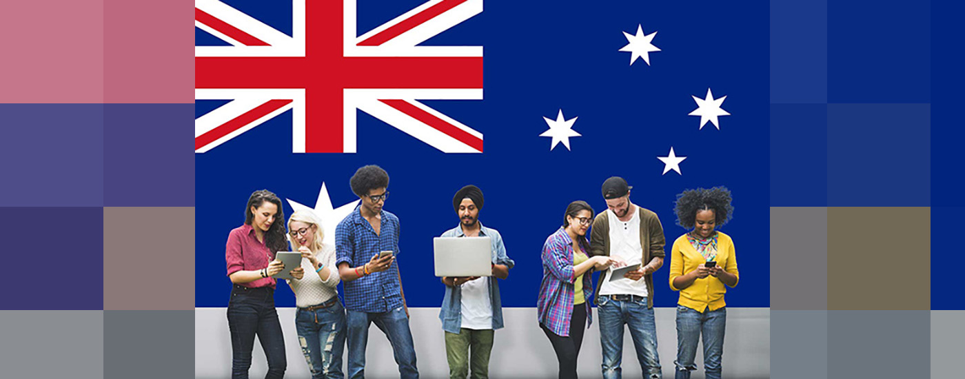 Australian flag in the background. Young people stand in front of it looking at their tablets, computers and phones.