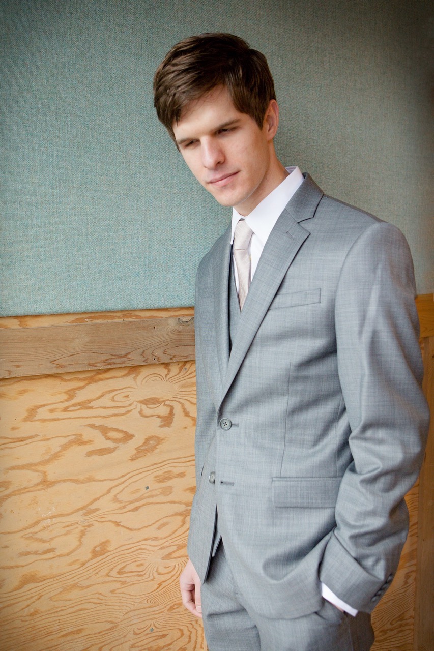 Mac Potts wears a grey suit with a beige tie.