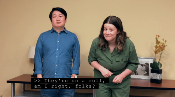 Roll-up captioning example. A man and woman stand side-by-side. The woman is doubled over and grinning at a joke she made while the man sighs. A roll-up caption in progress reads "They're on a roll, am I right, folks?"