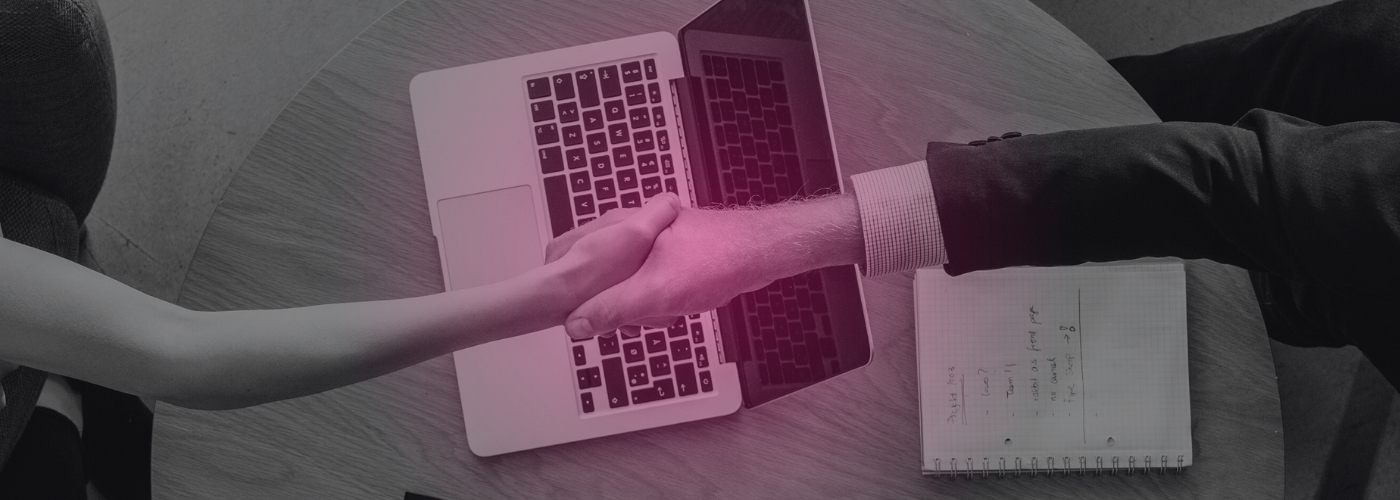 two people shake hands over a laptop