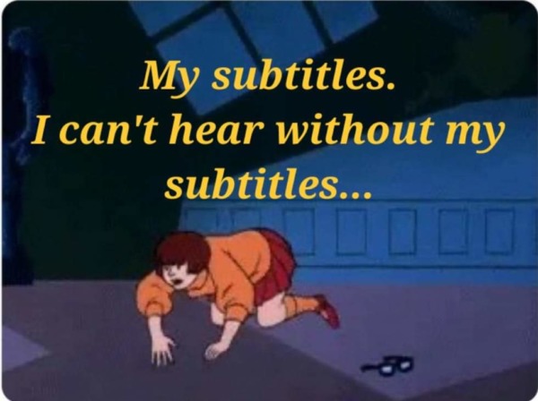 A person, Velma from "Scooby Doo", crawls around on the ground. Their glasses lay on the ground on the other side of them. Yellow italic text over the picture reads "My subtitles. I can't hear without my subtitles..."