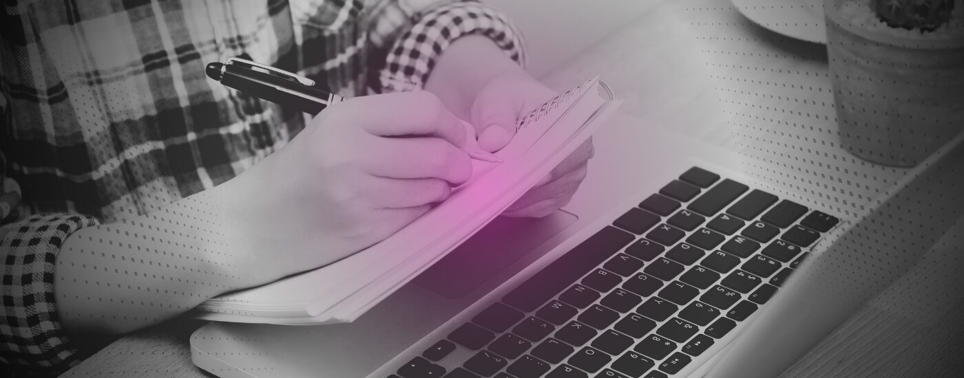 Person taking notes on notebook over a laptop
