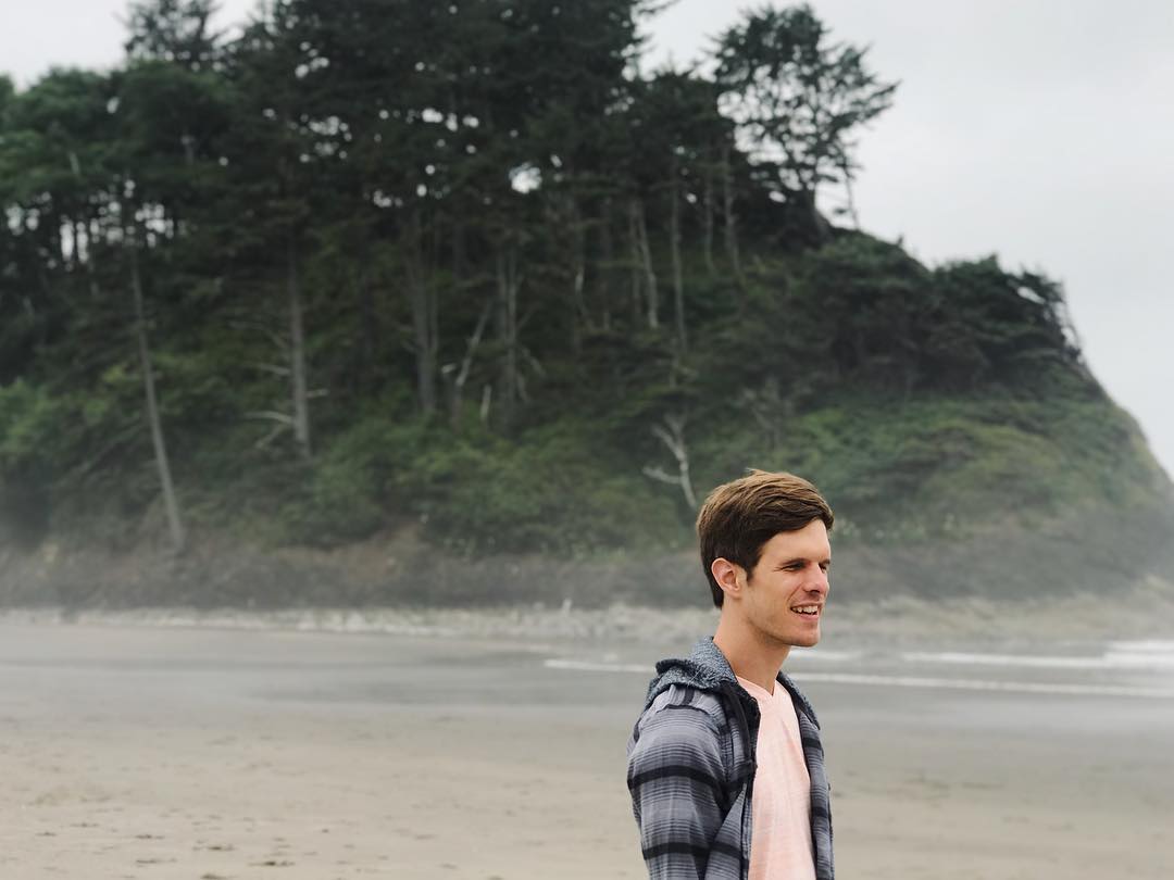 Mac Potts stands on a misty beach looking out towards the water.