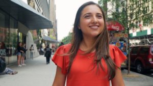Camila Chiriboga walks while wearing a red shirt and smiling