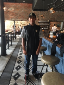 Marvin smiles while standing at a bar with Saints gear and a walking cane