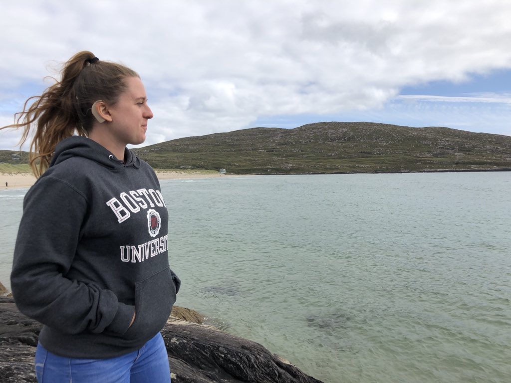 Alanna faces her body toward a beach, while wearing a Boston University sweater 
