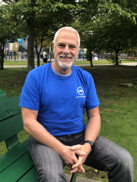 John Carroll, a white man in a blue t-shirt sitting on a park bench.