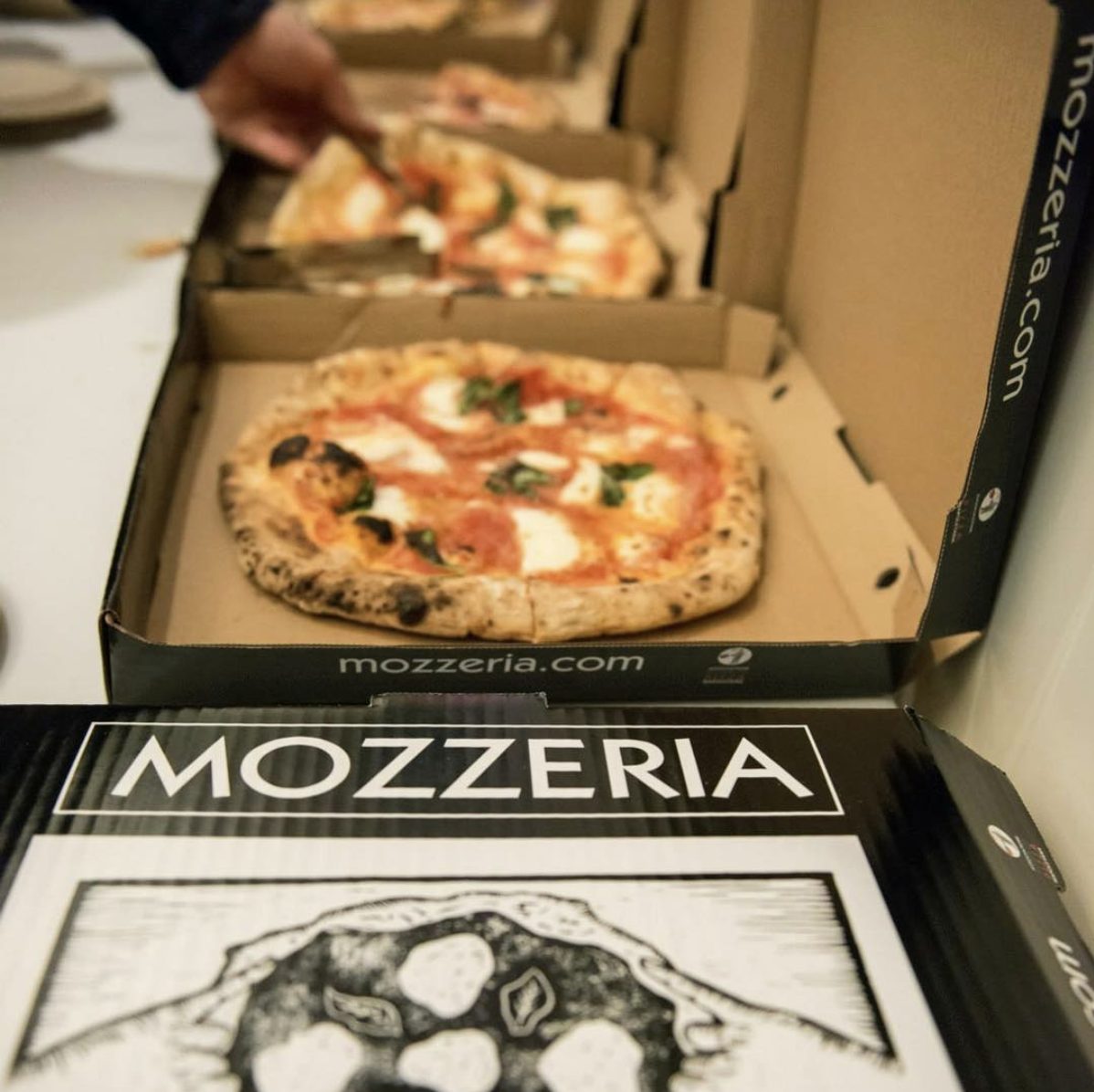 Mozzeria pizza boxes filled with fresh Margherita pizza.