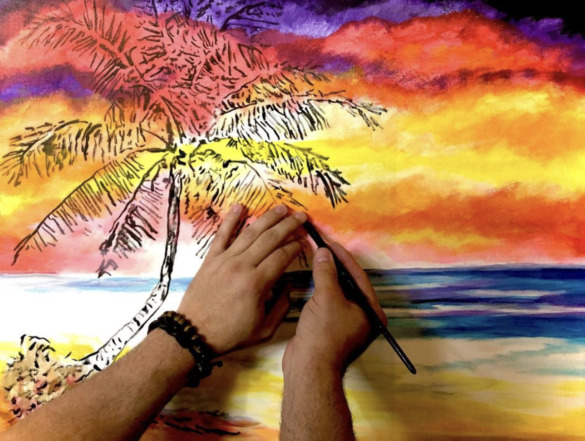 John Bramblitt's hands paint a sunset on the beach. His left hand touches the canvas and his right hand holds the paintbrush.