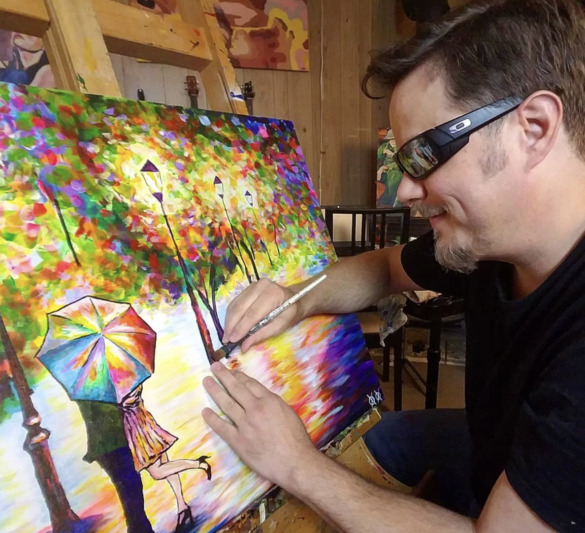 John Bramblitt works on a colorful painting of a man and woman standing under an umbrella.