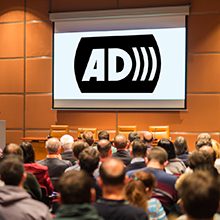 A group of people in a lecture hall looking at a projector screen that has the AD logo on it