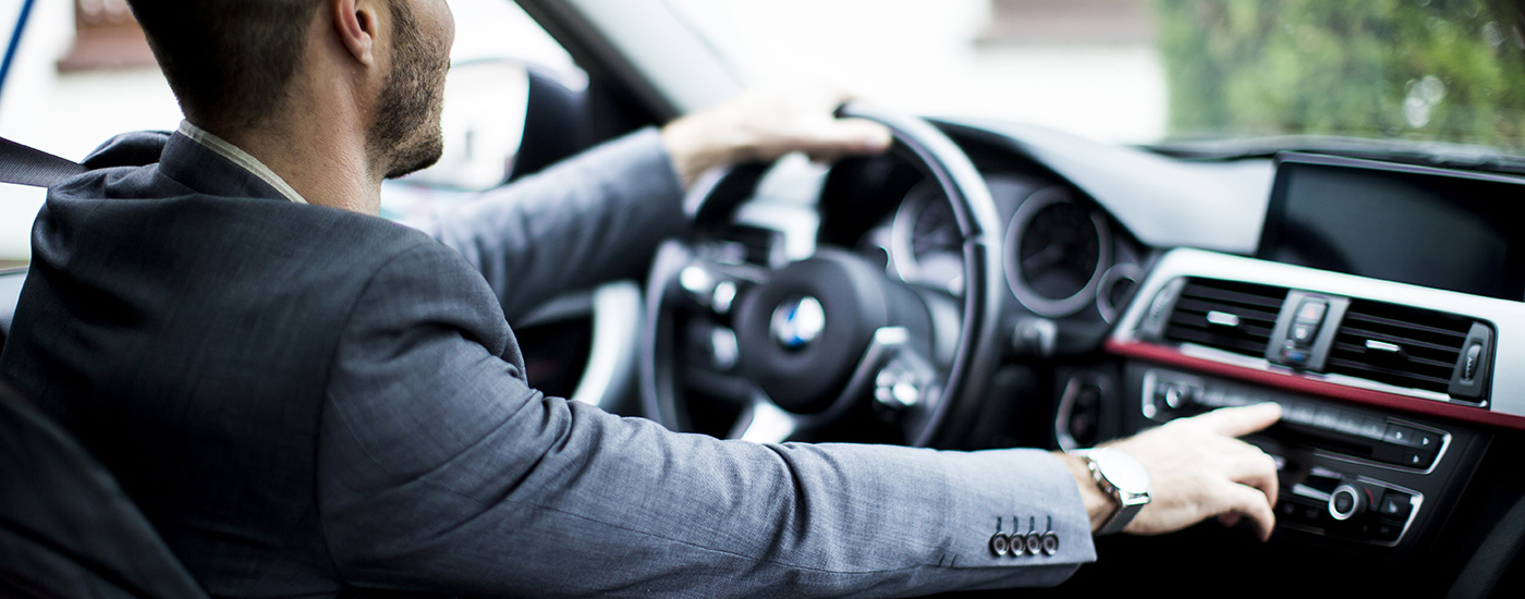 Man driving a car. One hand on the steering wheel and the other hand pressing a button on the main console.