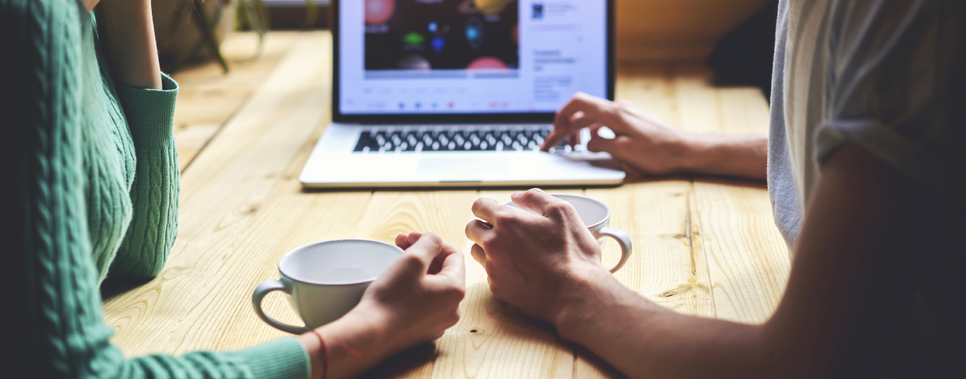 Two people sitting with coffee at a table together looking at a laptop with what appears to be a video showing on the screen