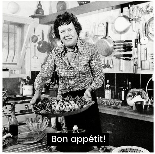 Julia Child holding plate a food. The caption reads bon appetit