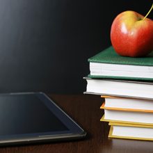 An apple on a stack of books next to an tablet