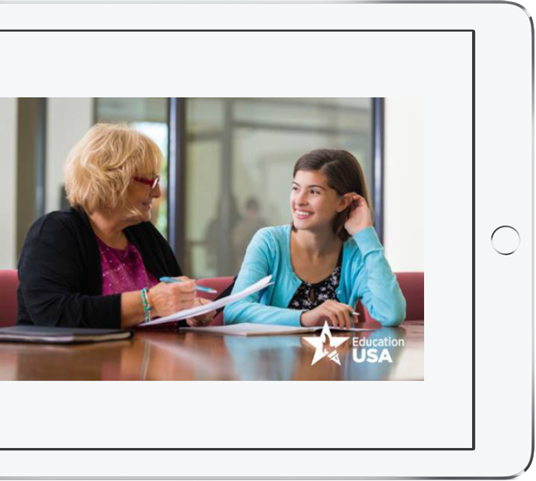 A photo of a young woman and an older woman smiling at each other while signing papers. Education USA watermark visible.
