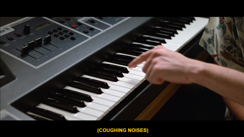 screenshot from the movie Ferris Bueller's Day Off. Ferris's hand is shown is playing a keyboard. The caption reads [coughing noises].