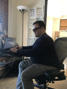 Joshua sits in a office chair while typing on his laptop