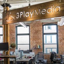 Entrance to inside of the 3Play Media office. Desks and a suspended wooden sign with 3Play Media written on it are shown.