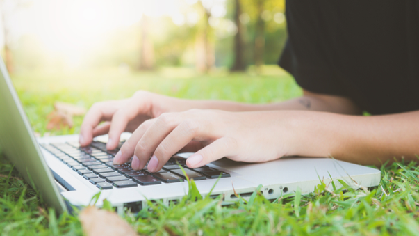 Student lays in grass and takes an online course on their laptop.