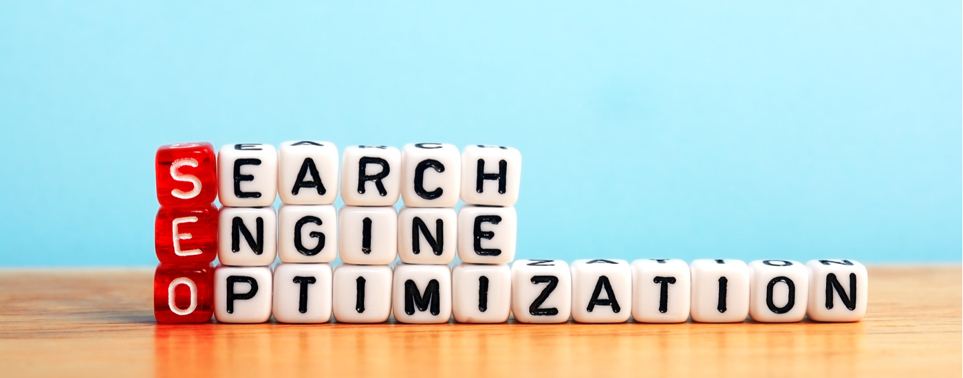 "Search Engine Optimization" spelled out in white and red alphabet beads, set on a shiny wooden table with a sky blue background