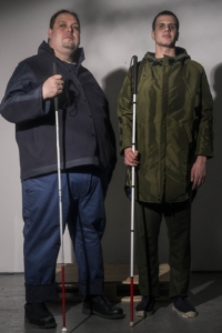 Gus poses with another model in a jacket, pants, and walking cane
