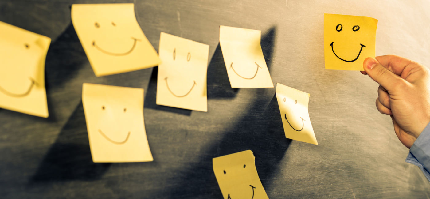 A man puts sticky notes on a blackboard. Every sticky note has a smily face drawn on it.