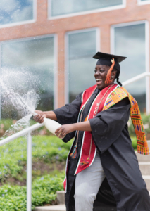 Bridgit pops a botle of champagne in her cap and gown in celebration of graduating