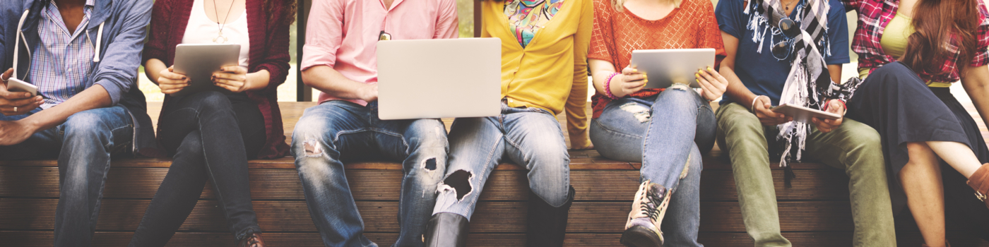 a group of young people pictured sitting on a bench with laptops and tablets